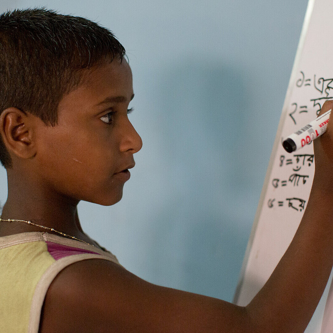 Ein Junge aus Bangladesch schreibt etwas auf ein Whiteboard