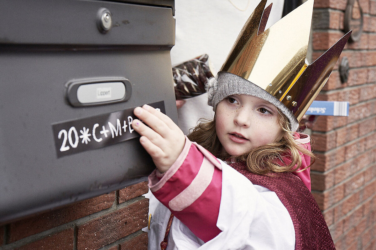 © Benne Ochs/Kindermissionswerk Eine Sternsingerin klebt den Segen an